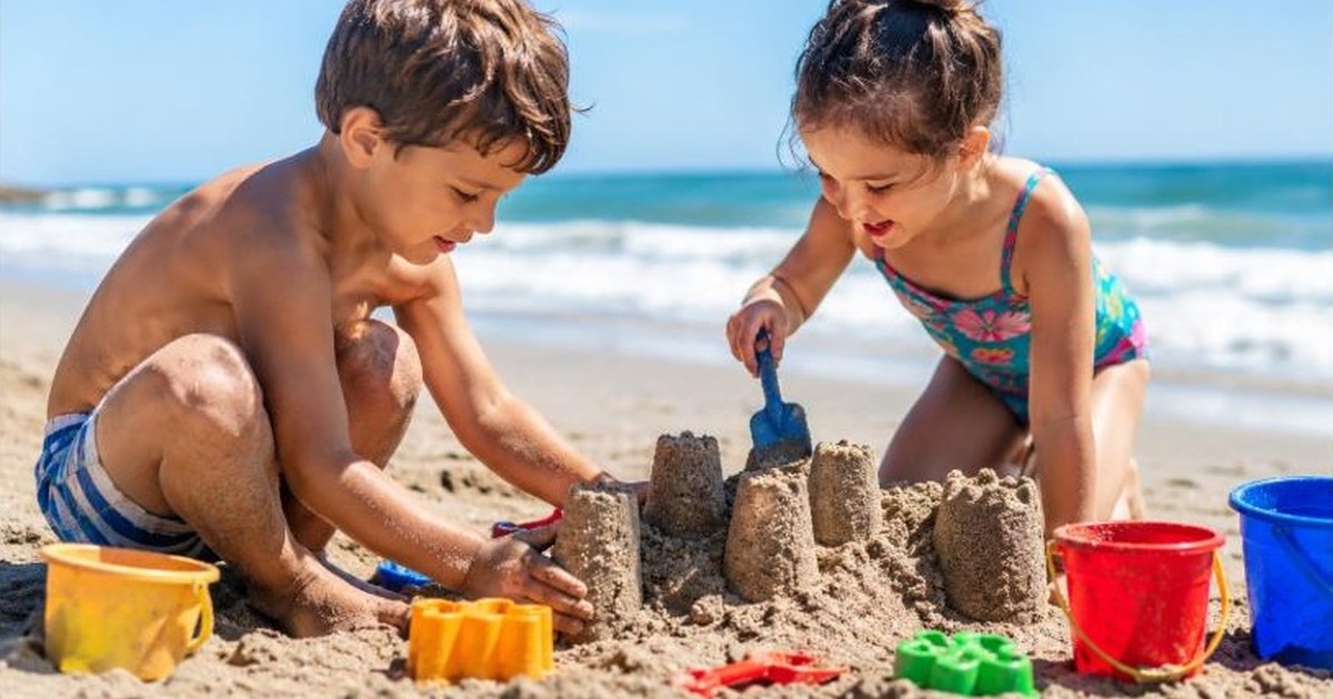 Two kids building a sandcastle together at the beach with colorful sand toys nearby